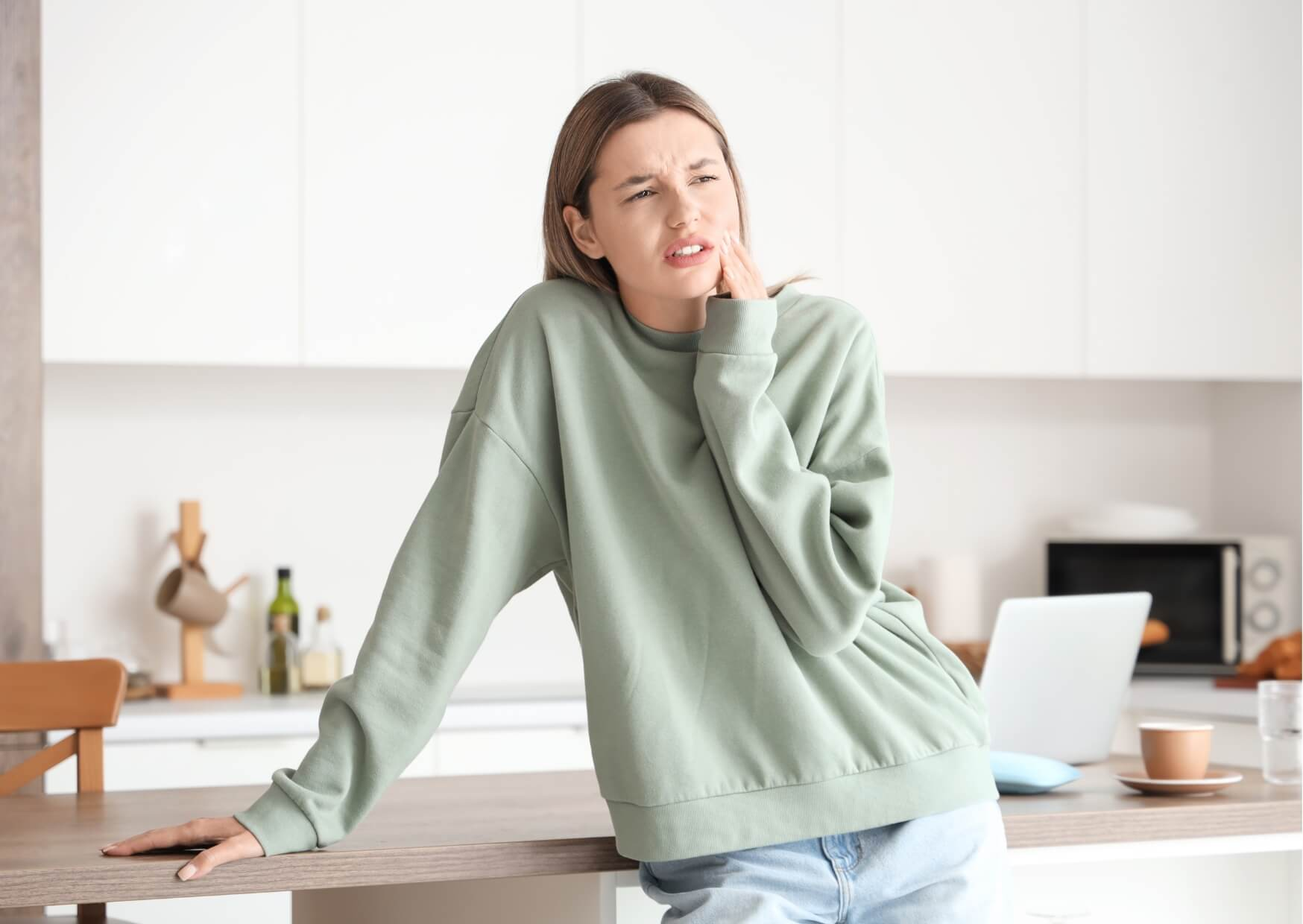 Woman holding her jaw in discomfort at home, illustrating the sharp pain and sensitivity that can occur with a cracked tooth.