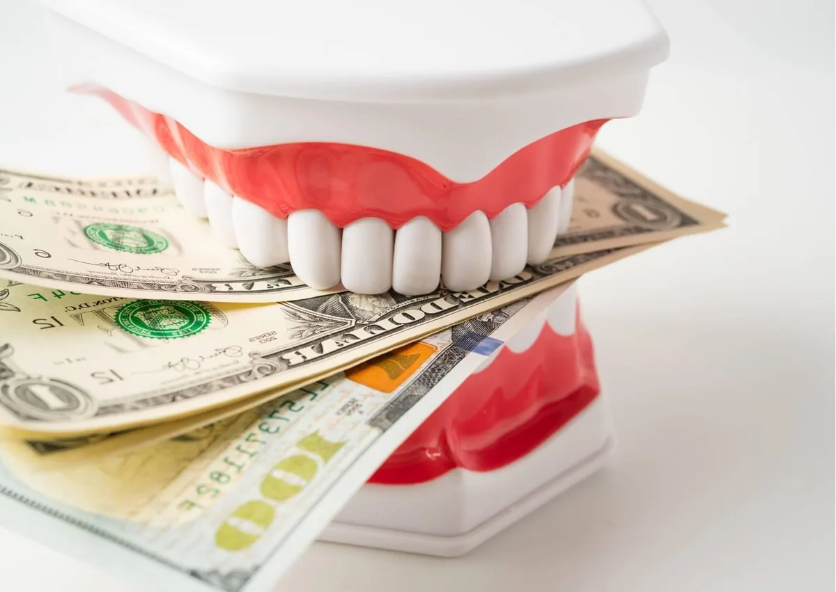 Dental model with cash representing the cost of cosmetic dentistry treatments.
