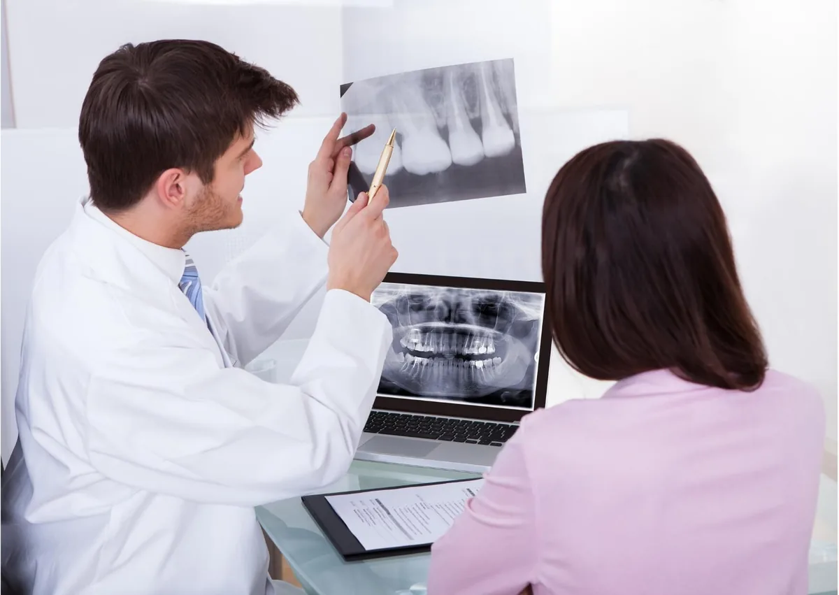 Dentist reviewing dental X-rays with a patient while explaining how many teeth humans have.