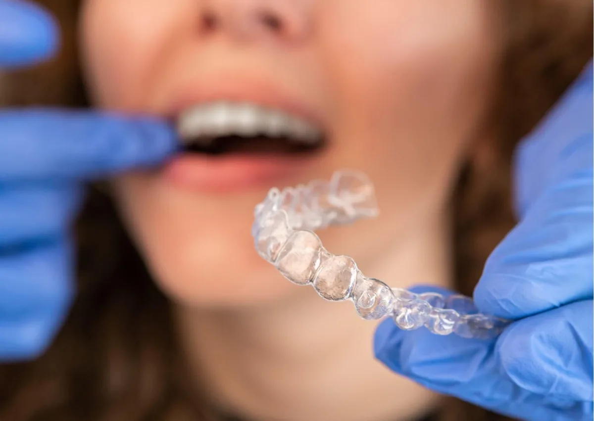 Dental professional holding a clear retainer while discussing retainer options and cost with a patient.