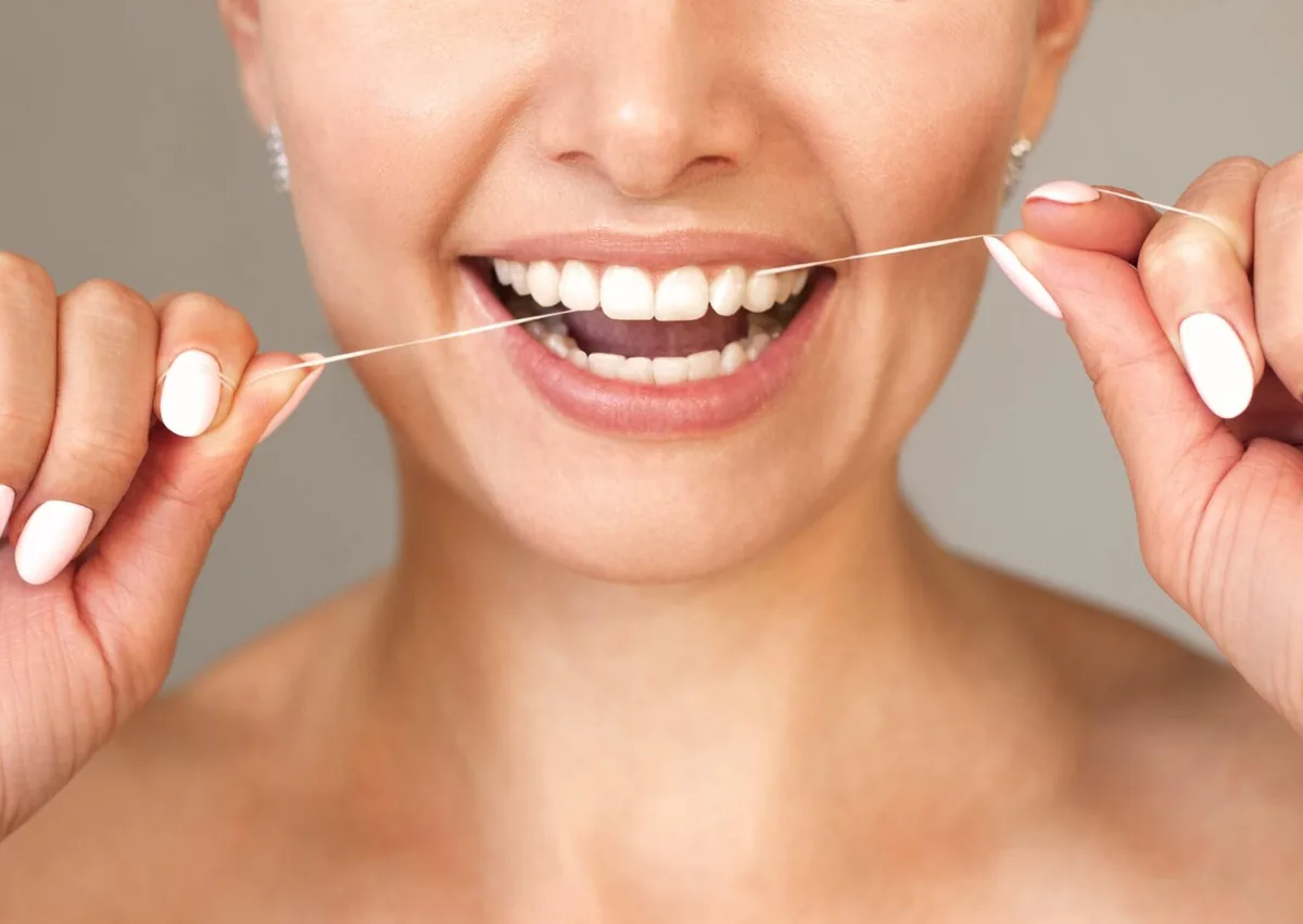 Woman flossing between her teeth to remove plaque and help prevent buildup along the gumline.